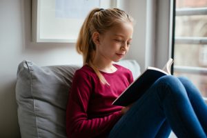Young teenage girl reading book in living room
