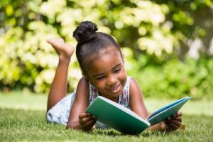 Little girl reading a book lying at park