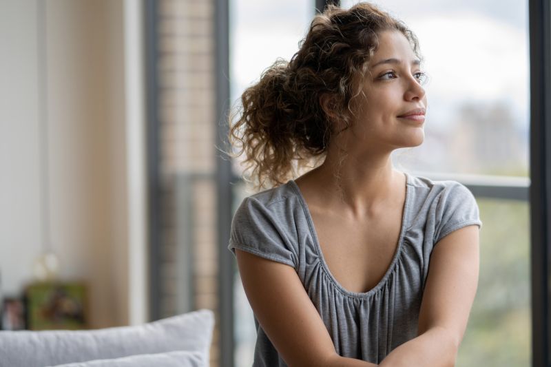 Woman looks out a window on a sunny day.
